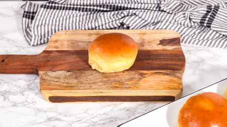 Step by step. Slicing freshly baked brioche bun on a wood cutting board.