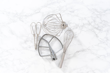 Flat lay. Variety of blending whisks on a marble countertop.