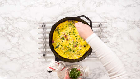 Flat lay. Step by step. Freshly baked spinach and ham frittata in cast iron skillet.の写真素材