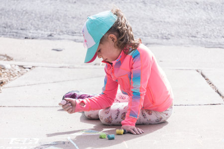 Little girl playing with chalk on a driveway in front of the house.