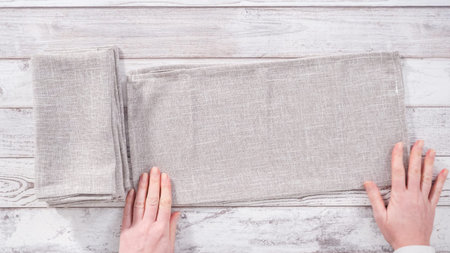 Step by step. Folding natural color linen dinner napkin on a wooden white table.の写真素材