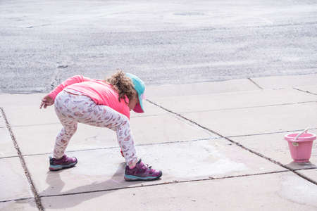 Little girl playing with chalk on a driveway in front of the house.の写真素材