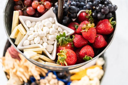 July 4th charcuterie board on a two-tiered serving metal stand filled with cheese, crackers, salami, and fresh fruitsの写真素材
