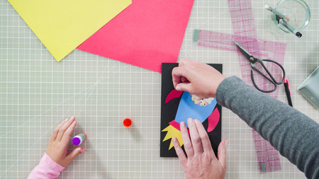 Flat lay. Little girl making a handmade Fathers Day card from construction paper.