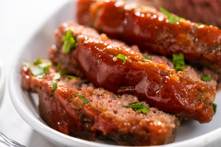 Slicing classic meatloaf with a sweet glaze on a white serving plateの写真素材