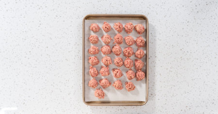 Flat lay. Scooping ground meat with dough scoop into a baking sheet lined with parchment paper to prepare oven-baked meatballs.の写真素材