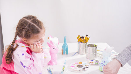 Little girl painting paper mache figurines with acrylic paint for her homeschooling art project.の写真素材
