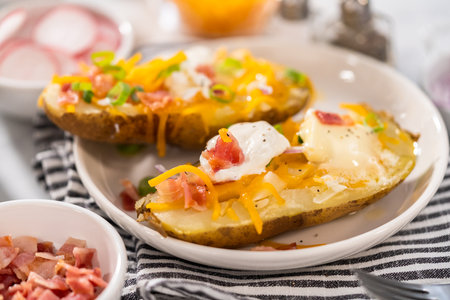 Pressure Cooker Baked Potatoes. Garnished large baked potatoes with butter, sour cream, cheese, and bacon bits on a white plate.の写真素材