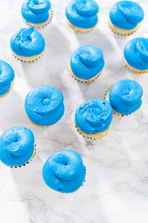 Frosting mini vanilla cupcakes with buttercream frosting to make an American flag mini cupcake cake.の写真素材