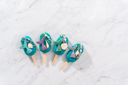 Flat lay. Mermaid cakesicles with drizzled chocolate, chocolate mermaid tails, seashells, and sprinkles.の写真素材