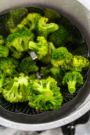 Steaming fresh broccoli in a cooking pot with a steamer basket to prepare steamed broccoli.の写真素材