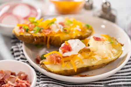 Pressure Cooker Baked Potatoes. Garnished large baked potatoes with butter, sour cream, cheese, and bacon bits on a white plate.の写真素材