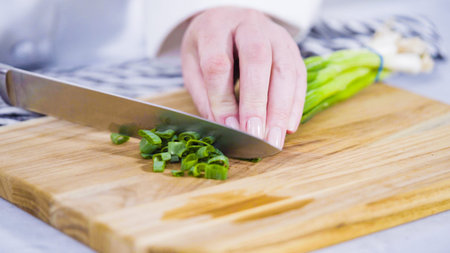 Step by step. Chopping organic green onions on a wood cutting board.