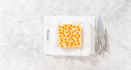 Flat lay. Scoring candy corn fudge using a parchment paper template for cutting into small pieces.