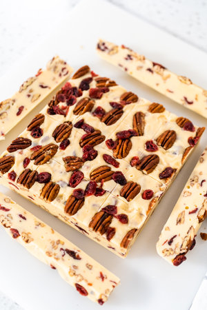 Cutting white chocolate cranberry pecan fudge into small pieces on a white cutting board.の写真素材