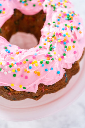 Funfettti bundt cake frosted with pink vanilla buttercream frosting and decorated with rainbow...