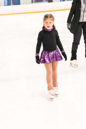 Little girl practicing figure skating on indoor ice skating rink.