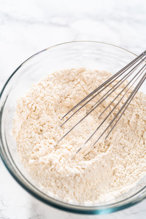 Mixing dry ingredients with a hand whisk in a large glass mixing bowl to bake mini Easter bread...