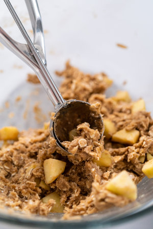 Scooping cookie dough into the baking sheet lined with parchment paper to bake apple oatmeal...