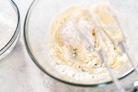 Mixing ingredients with a hand mixer in a large mixing bowl to make cream cheese frosting for carrot...