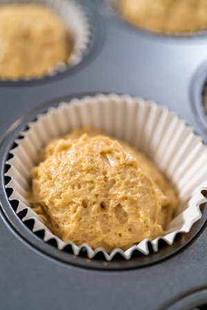 Scooping cupcake batter with dough scoop into a baking cupcake pan with liners to bake dulce de leche cupcakes.の写真素材