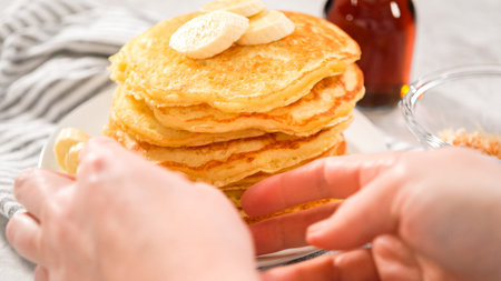 Step by step. Eating freshly baked coconut banana pancakes garnished with sliced bananas and toasted...