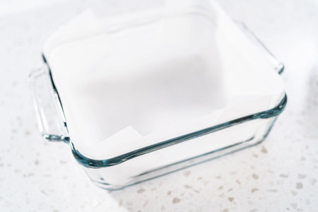 Lining glass baking pan with parchment paper sheet to prepare white chocolate cranberry pecan fudge.の写真素材