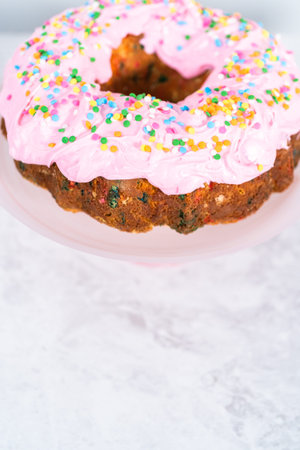 Funfettti bundt cake frosted with pink vanilla buttercream frosting and decorated with rainbow sprinkles.の写真素材