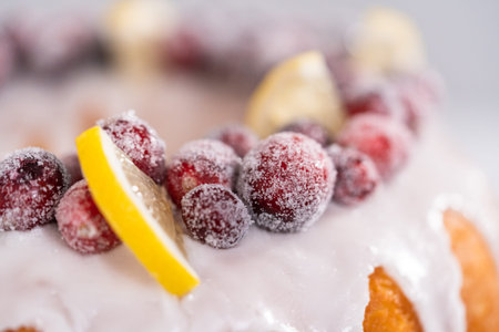 Lemon cranberry bundt cake decorated with sugar cranberries and lemon wedges on a cake stand.の写真素材