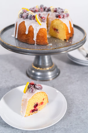 Sliced lemon cranberry bundt cake decorated with sugar cranberries and lemon wedges on a cake stand.