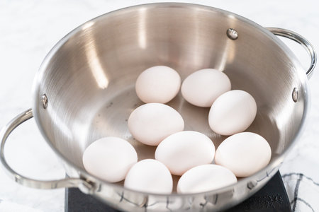 Boiling white eggs in a cooking pot to prepare hard-boiled eggs.の写真素材