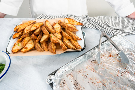 Freshly baked potato wedges with spices on a white serving tray.の写真素材