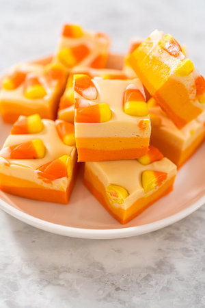 Homemade candy corn fudge square pieces on a white plate.の写真素材