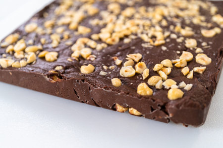 Removing chocolate hazelnut fudge from a square cheesecake pan lined with parchment.