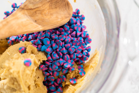 Mixing in rainbow chocolate chips with cookie dough to bake unicorn chocolate chip cookies.