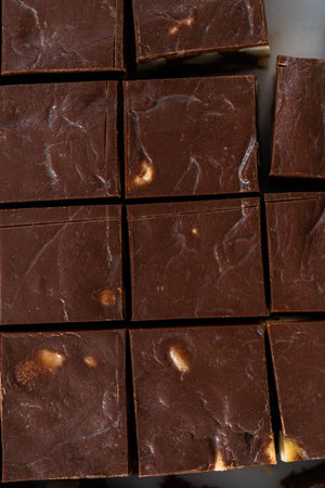 Cutting chocolate macadamia fudge with a large kitchen knife into square pieces on a white cutting...