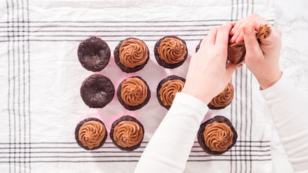 Flat lay. Step by step. Piping chocolate ganache frosting on top of chocolate cupcakes.の写真素材
