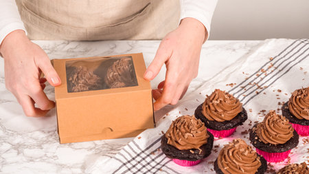 Step by step. Packaging chocolate cupcakes with chocolate ganache frosting into a paper cupcake box.の写真素材