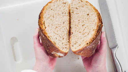 Flat lay. Slicing freshly baked sourdough wheat bread on a white cutting board.