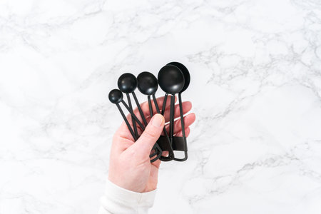 Flat lay. Black metal measuring spoons for baking on a marble countertop.の写真素材