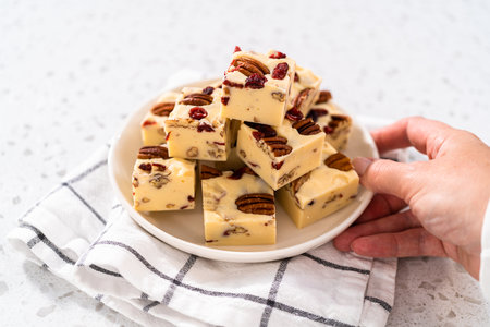 Homemade white chocolate cranberry pecan fudge pieces on a white ceramic plate.の写真素材