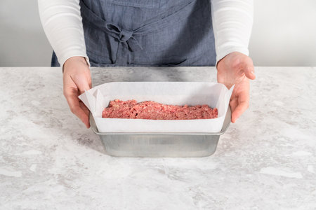 Preparing classic meatloaf in a loaf pan lined with parchment paper.の写真素材