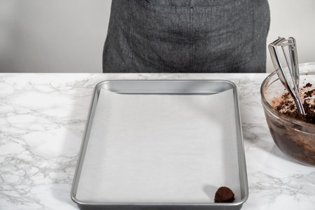 Scooping cookie dough with a small dough scoop into a baking sheet lined with parchment paper to...