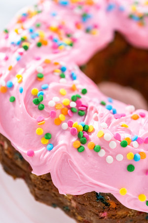 Close up view. Funfettti bundt cake frosted with pink vanilla buttercream frosting and decorated with rainbow sprinkles.の写真素材