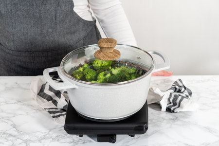 Steaming fresh broccoli in a cooking pot with a steamer basket to prepare steamed broccoli.の写真素材