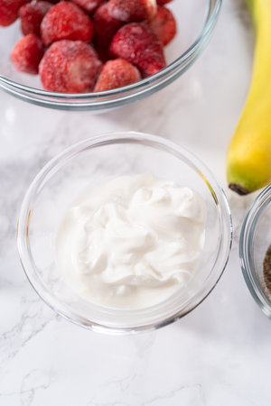 Measured ingredients in a glass mixing bowl to prepare a strawberry banana smoothie.の写真素材