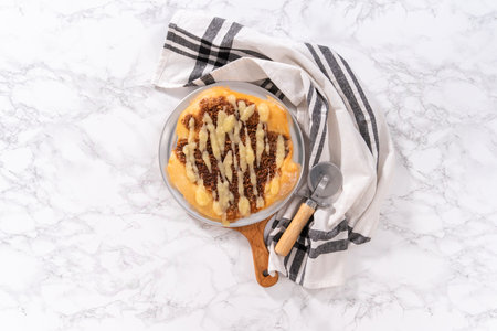 Flat lay. Freshly baked cinnamon dessert pizza with cream cheese drizzle.の写真素材