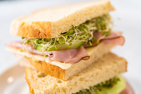 Stack of ham, cucumber, and sprout sandwiches on the white plateの写真素材