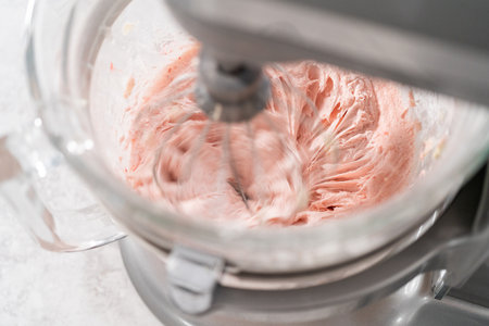Whipping strawberry buttercream frosting in a stand-alone electric mixer with a whisk attachment.の写真素材