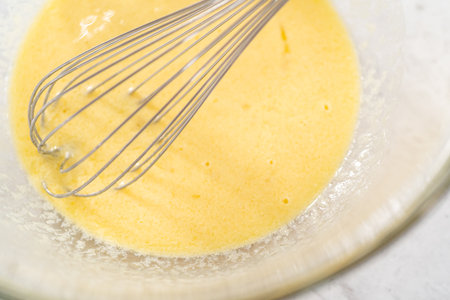 Mixing ingredients in a glass mixing bowl with a blending whisk to bake chocolate strawberry cupcakes.の写真素材